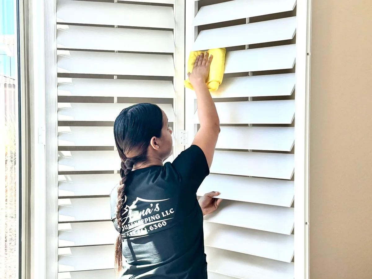 Anna's Housekeeping cleaner dusting plantation blinds in a Buckeye, Arizona home